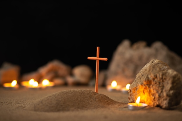 Pequeña tumba con piedras y velas encendidas sobre una superficie oscura