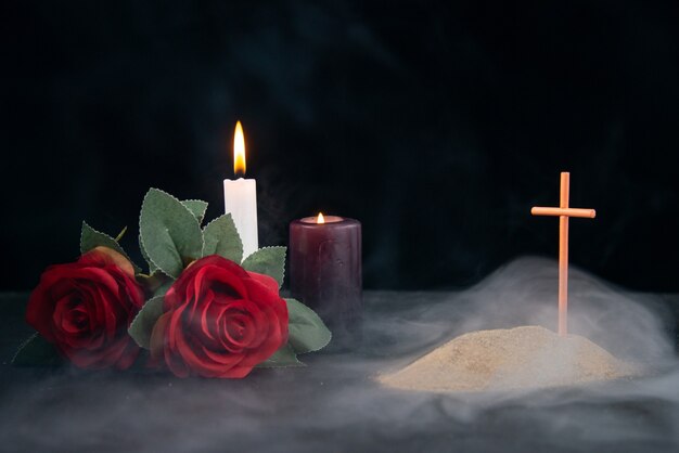 Pequeña tumba con velas y flores como recuerdo en superficie oscura