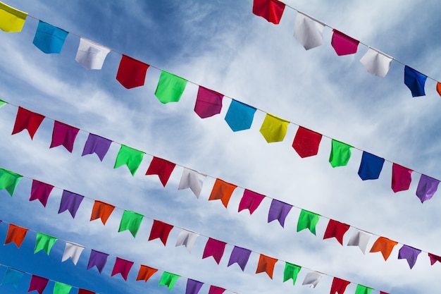 Pequeñas banderas coloridas lindas en la cuerda que cuelga afuera para el día de fiesta con el cielo azul brillante fondo blanco de las nubes. Italia, Cerdeña.