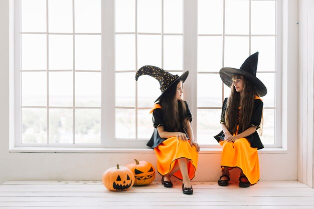 Pequeñas brujas de Halloween hablando en el alféizar de la ventana