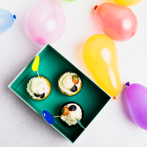 Pequeñas magdalenas en caja verde con globos.