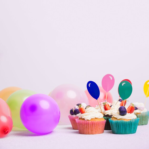 Pequeñas magdalenas con globos en mesa blanca