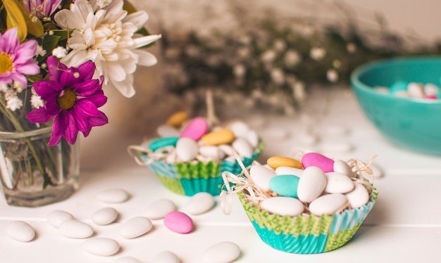 Pequeñas piedras brillantes en canastas cerca de jarrón con ramo de flores