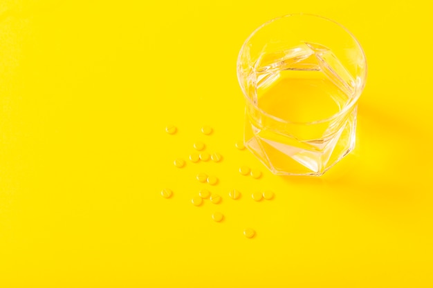 Pequeñas tabletas de medicina y vaso de agua sobre el fondo amarillo