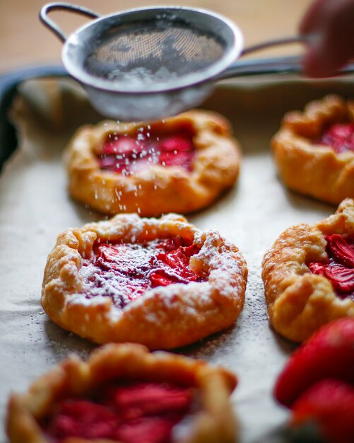 Pequeñas tartas rústicas de tarta de fresa con azúcar en polvo en la bandeja del horno