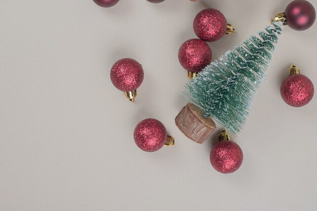 Pequeño árbol de Navidad con bolas de Navidad rojas sobre superficie blanca