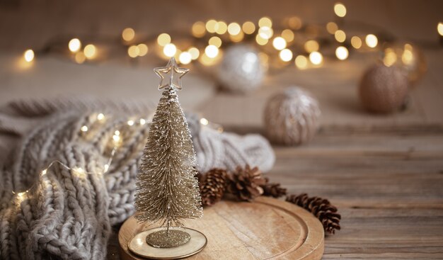 Pequeño árbol de Navidad brillante decorativo de cerca sobre un fondo de luces borrosas con bokeh en colores cálidos.