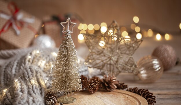 Pequeño árbol de Navidad brillante decorativo en primer plano sobre un fondo borroso de adornos navideños, guirnaldas y luces bokeh.