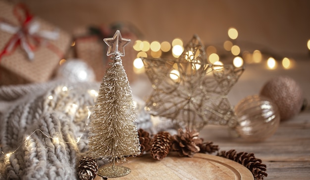 Pequeño árbol de Navidad brillante decorativo en primer plano sobre un fondo borroso de adornos navideños, guirnaldas y luces bokeh.