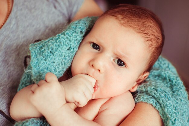 El pequeño bebé enojado miente en los brazos de madre