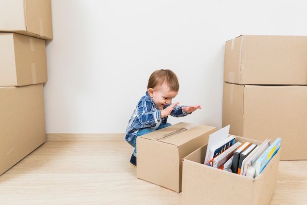 Pequeño bebé feliz que juega con las cajas de cartón en el nuevo hogar