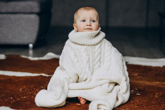 Pequeño bebé lindo que se sienta en piso en suéter caliente