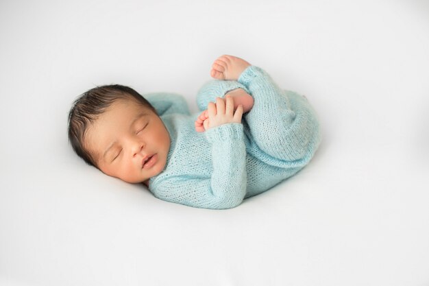 Pequeño bebé recién nacido acostado en una silla blanca en pijamas de ganchillo azul