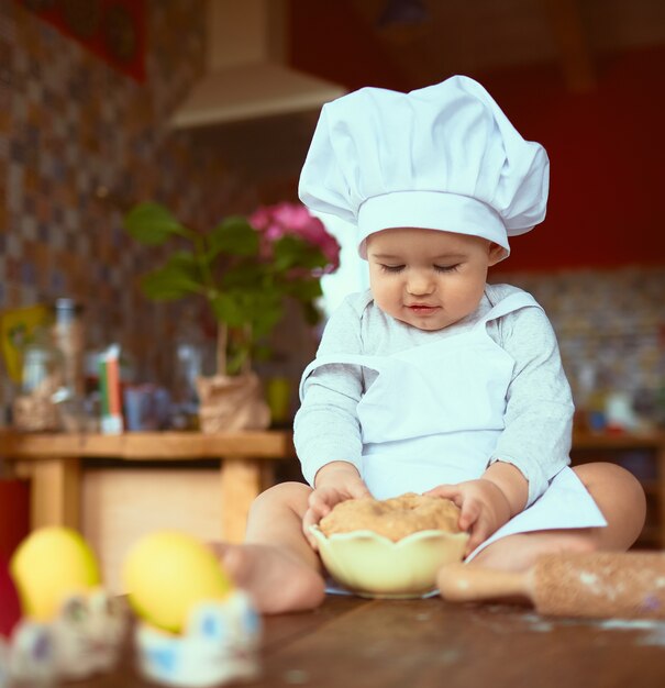 El pequeño bebé sentado en la mesa y jugando con la masa