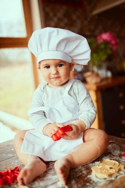 El pequeño bebé se sienta en la mesa cerca de la masa