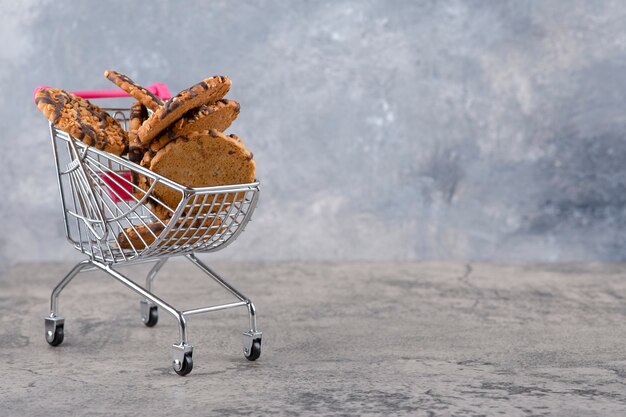 Un pequeño carrito rosa con galletas de avena saludables colocadas sobre una mesa de piedra.