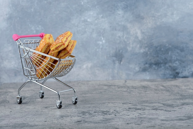 Un pequeño carrito rosa de sabrosas galletas colocado sobre una mesa de mármol.