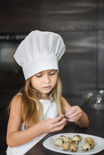 Pequeño cocinero lindo que hace pis la cáscara de huevos de codorniz en cocina