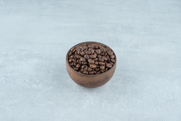 Un pequeño cuenco de madera con granos de café sobre fondo blanco. Foto de alta calidad