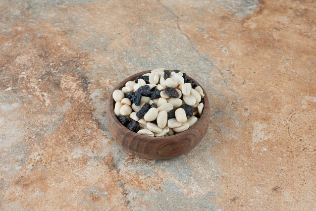 Un pequeño cuenco de madera lleno de pasas y nueces sobre fondo de mármol