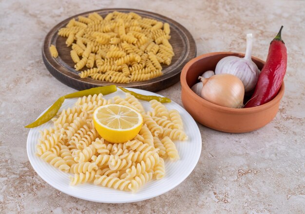 Pequeño cuenco de verduras y porciones de pasta en estado crudo y cocido sobre superficie de mármol.