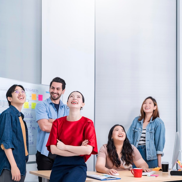 Pequeño emprendedor asiático inteligente de pie retrato confiado con amigos socios reunión informal lluvia de ideas con pizarra blanca y análisis de gráficos de papel de finanzas comerciales en el fondo de la oficina