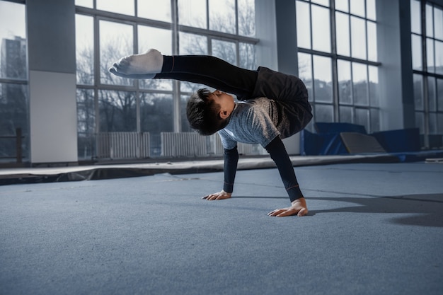 Pequeño gimnasta masculino entrenando en gimnasio, flexible y activo