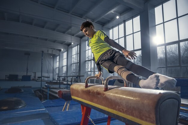 Pequeño gimnasta masculino entrenando en gimnasio, flexible y activo