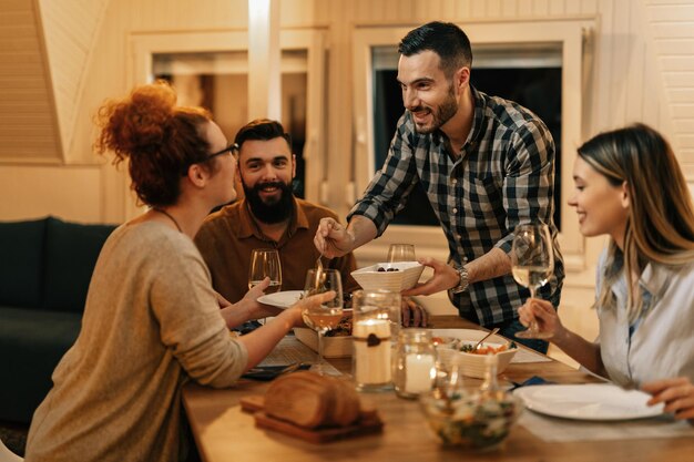 Pequeño grupo de amigos felices comiendo juntos en la mesa de comedor El foco está en el hombre sirviendo comida