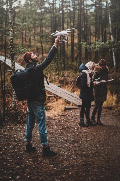 Un pequeño grupo de personas está disfrutando de su caminata en el parque forestal de otoño, uno de ellos está haciendo una foto a través de un dron.