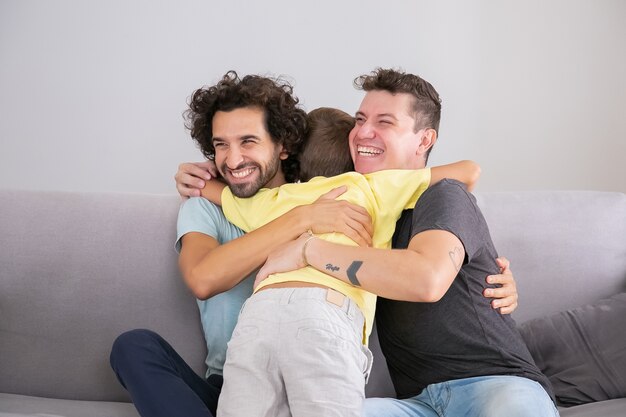 Pequeño hijo abrazando a dos padres guapos felices en casa. Tiro medio. Concepto de familia y paternidad feliz