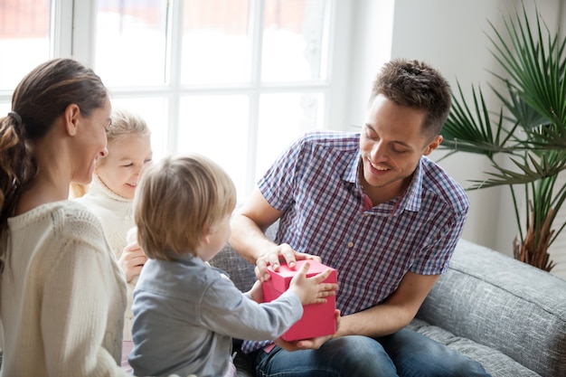 Pequeño hijo presentando un regalo para papá, familia celebrando el día del padre.