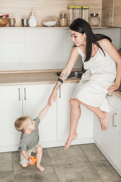 Pequeño hijo tirando de su madre sentada en el mostrador de la cocina