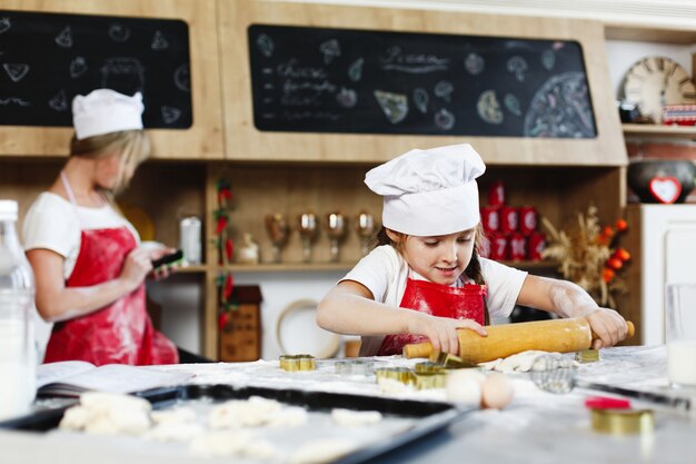 Pequeño jefe Una chica encantadora se divierte haciendo galletas de masa en una cocina acogedora