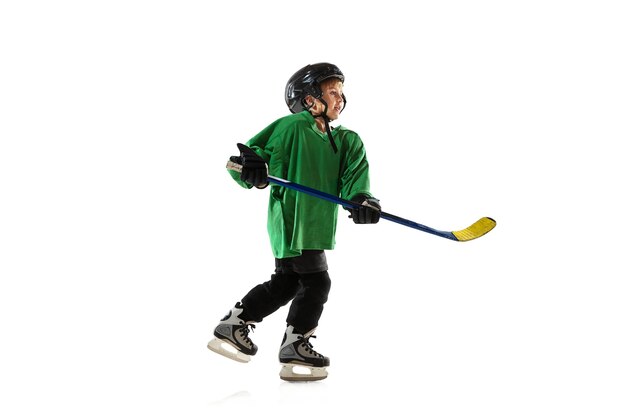 Pequeño jugador de hockey con el palo en la cancha de hielo, fondo blanco del estudio. Deportista con equipo y casco, practicando, entrenando. Concepto de deporte, estilo de vida saludable, movimiento, movimiento, acción.