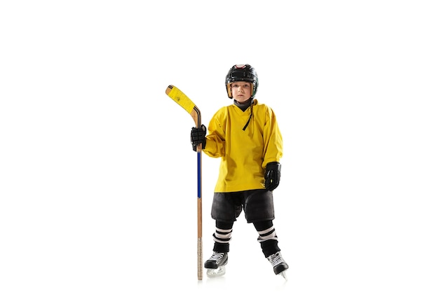 Pequeño jugador de hockey con el palo en la cancha de hielo y la pared blanca del estudio