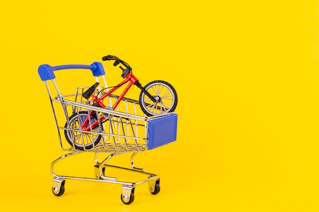 Pequeño juguete de bicicleta en el carrito de compras sobre fondo amarillo.