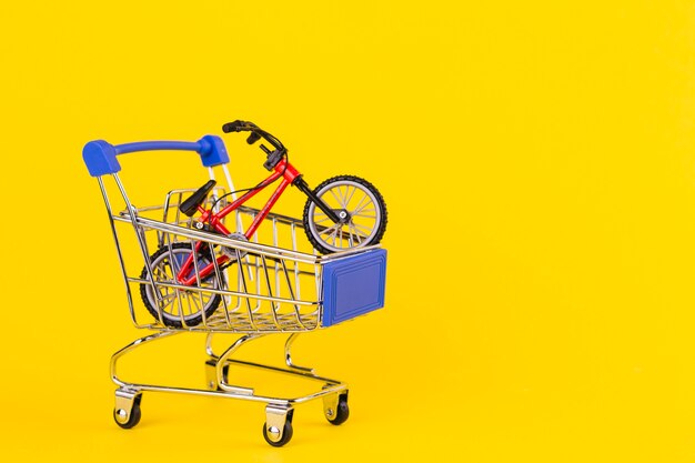 Pequeño juguete de bicicleta en el carrito de compras sobre fondo amarillo.