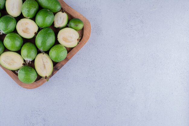 Pequeño montón de feijoas envuelto en una bandeja de madera sobre fondo de mármol. Foto de alta calidad