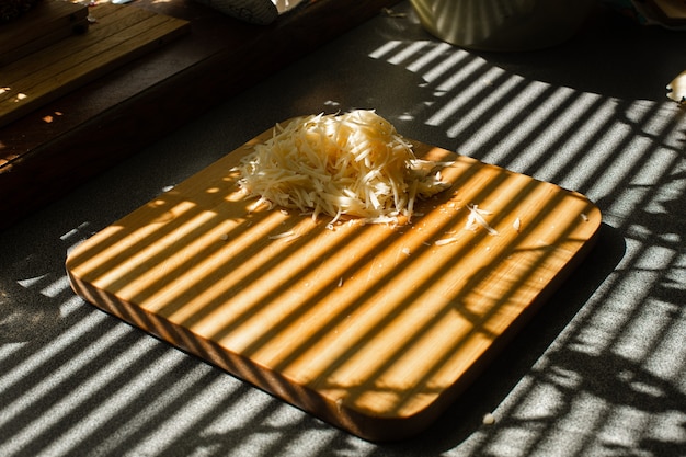 Un pequeño montón de queso fresco rallado se encuentra sobre una tabla de madera en la cocina