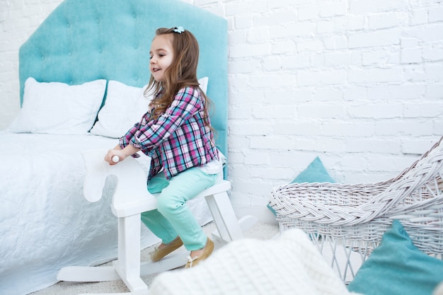 Pequeño niño monta caballo blanco de madera en el cuarto azul