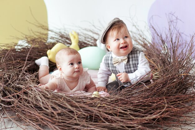 Pequeño niño y niña sentada en nido natural con coloridos huevos de Pascua.