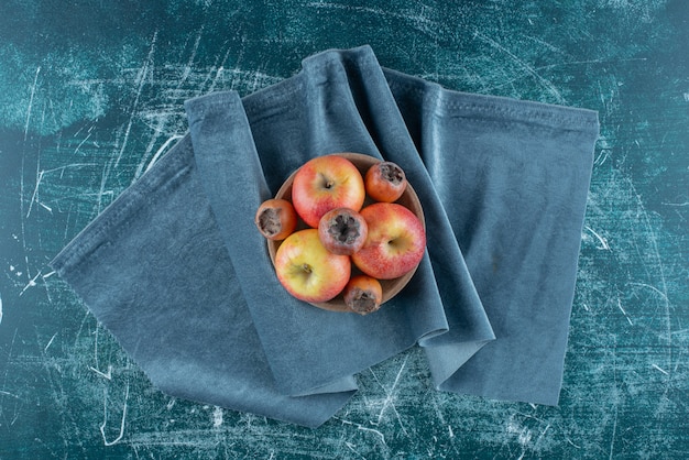 Foto gratuita un pequeño paquete de nísperos y manzanas en el cuenco, sobre la toalla, sobre el fondo azul. foto de alta calidad