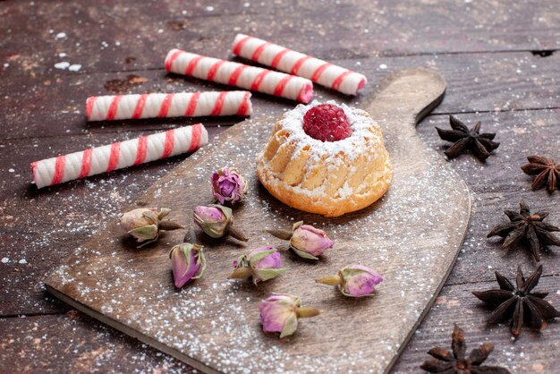 Pequeño pastel cremoso con frambuesa junto con caramelos de palo rosa sobre un escritorio de madera marrón, pastel de hornear de azúcar dulce caramelo