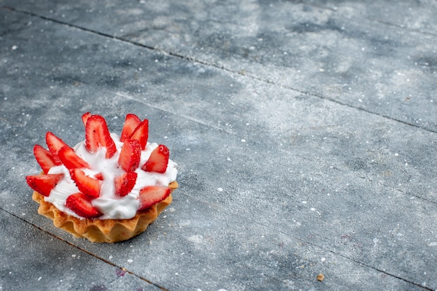 Pequeño pastel cremoso con fresas en rodajas sobre un escritorio de madera gris, pastel de frutas y bayas de color dulce