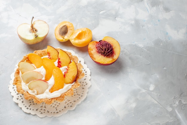 pequeño pastel cremoso con frutas en rodajas y crema blanca junto con albaricoques frescos, duraznos en un escritorio con luz blanca, pastel de frutas, galletas, galletas horneadas