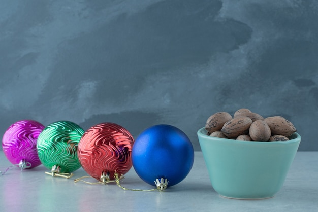 Un pequeño plato azul lleno de nueces con bolas de Navidad sobre fondo de mármol. Foto de alta calidad