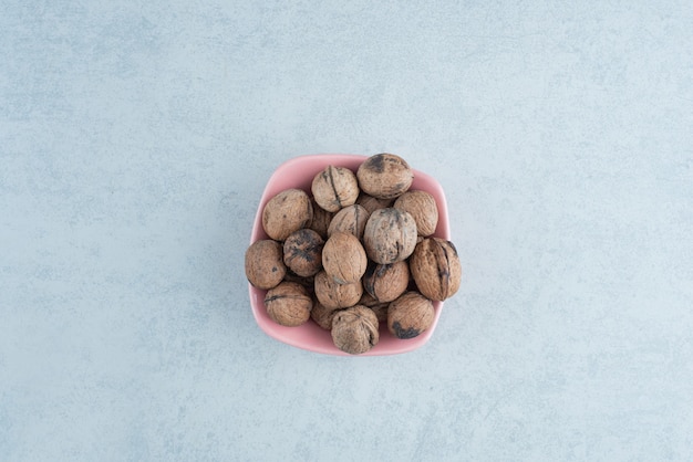 Foto gratuita un pequeño plato rosa lleno de nueces sobre fondo de mármol. foto de alta calidad