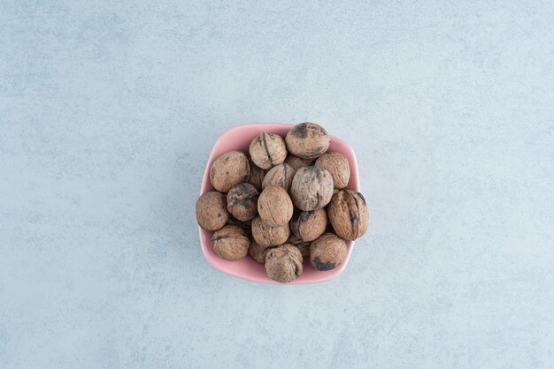 Un pequeño plato rosa lleno de nueces sobre fondo de mármol. Foto de alta calidad