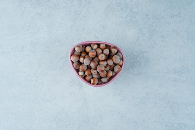 Un pequeño plato rosa lleno de nueces sobre fondo de mármol. Foto de alta calidad